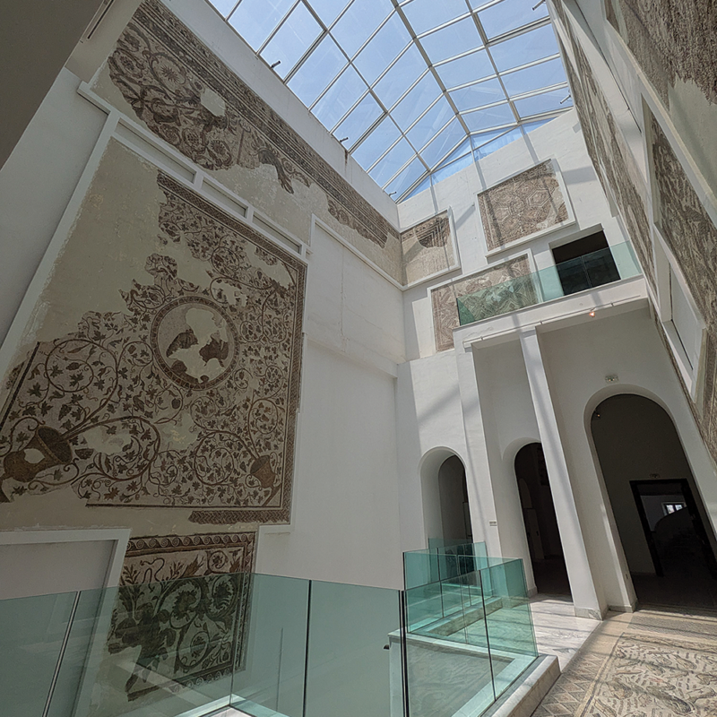 Mosaics displayed on the walls and floor of a sun-filled hallway.